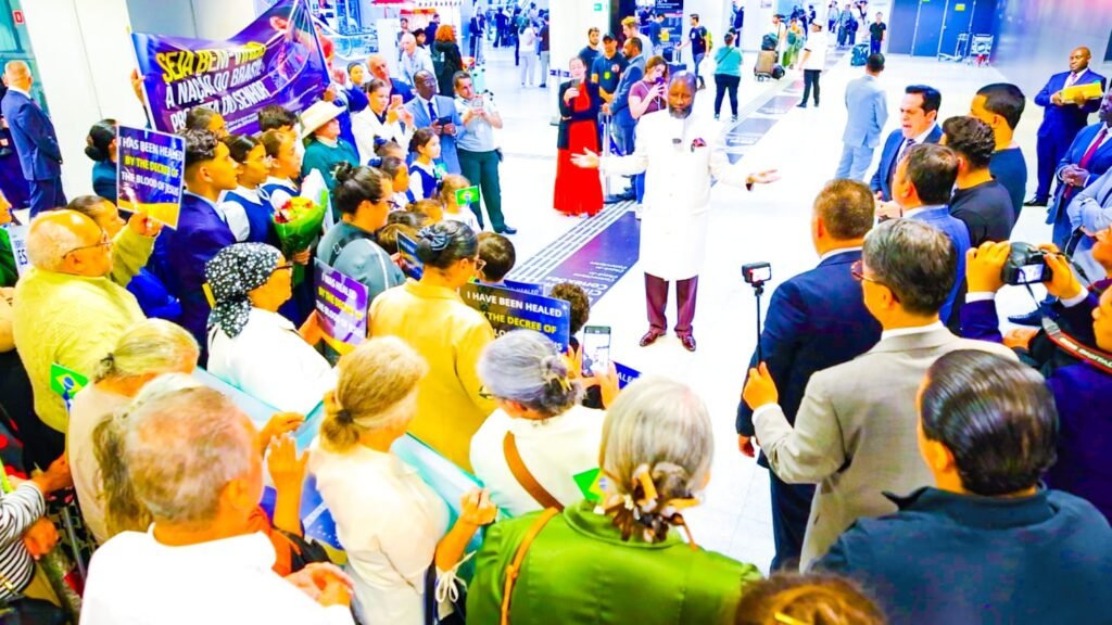 Prophet Dr. David Owuor greets the faithful on arrival at São Paulo airport, beneath a Portuguese welcome banner and Brazilian flags